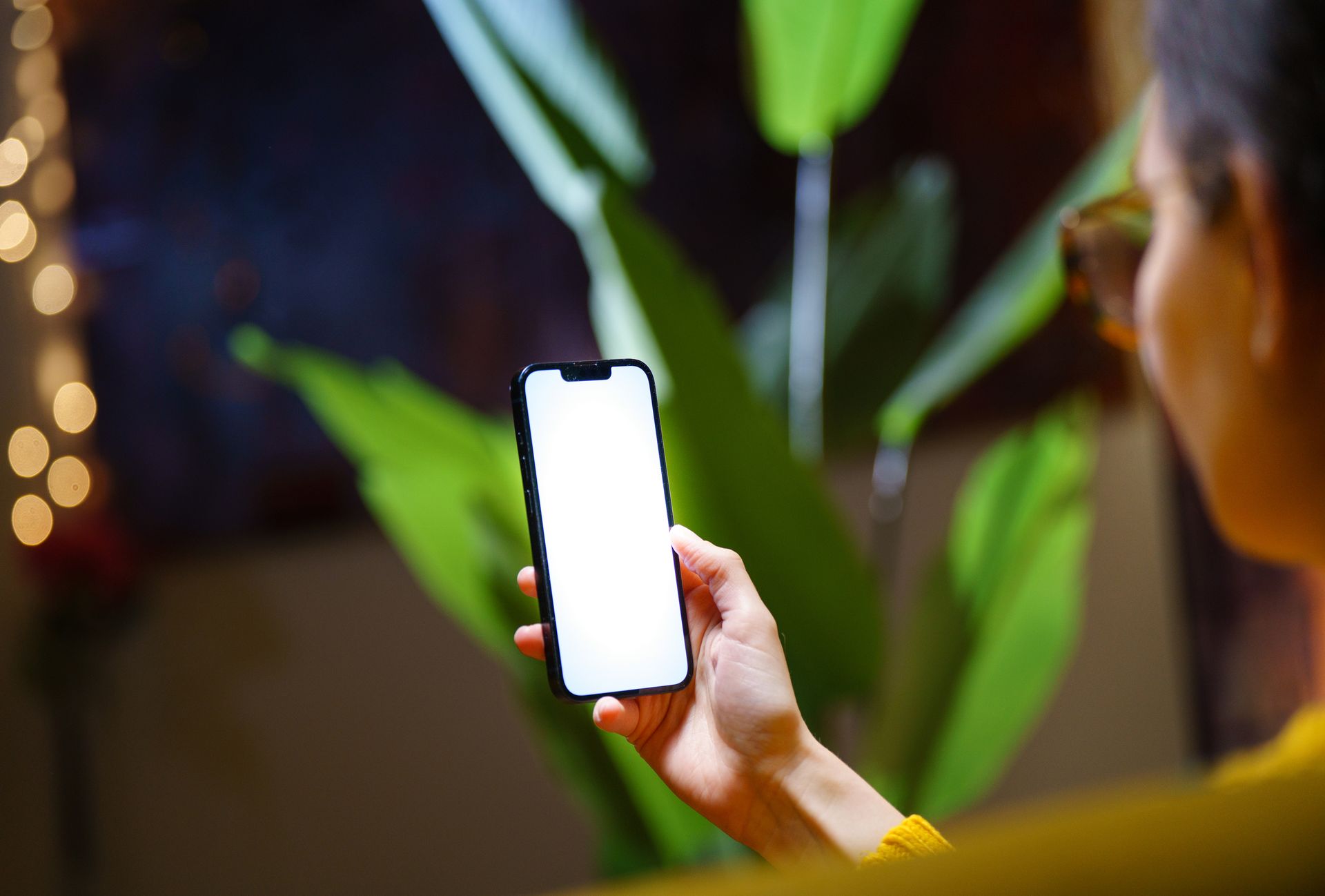 A person holding a smartphone with a blank screen near indoor plants.