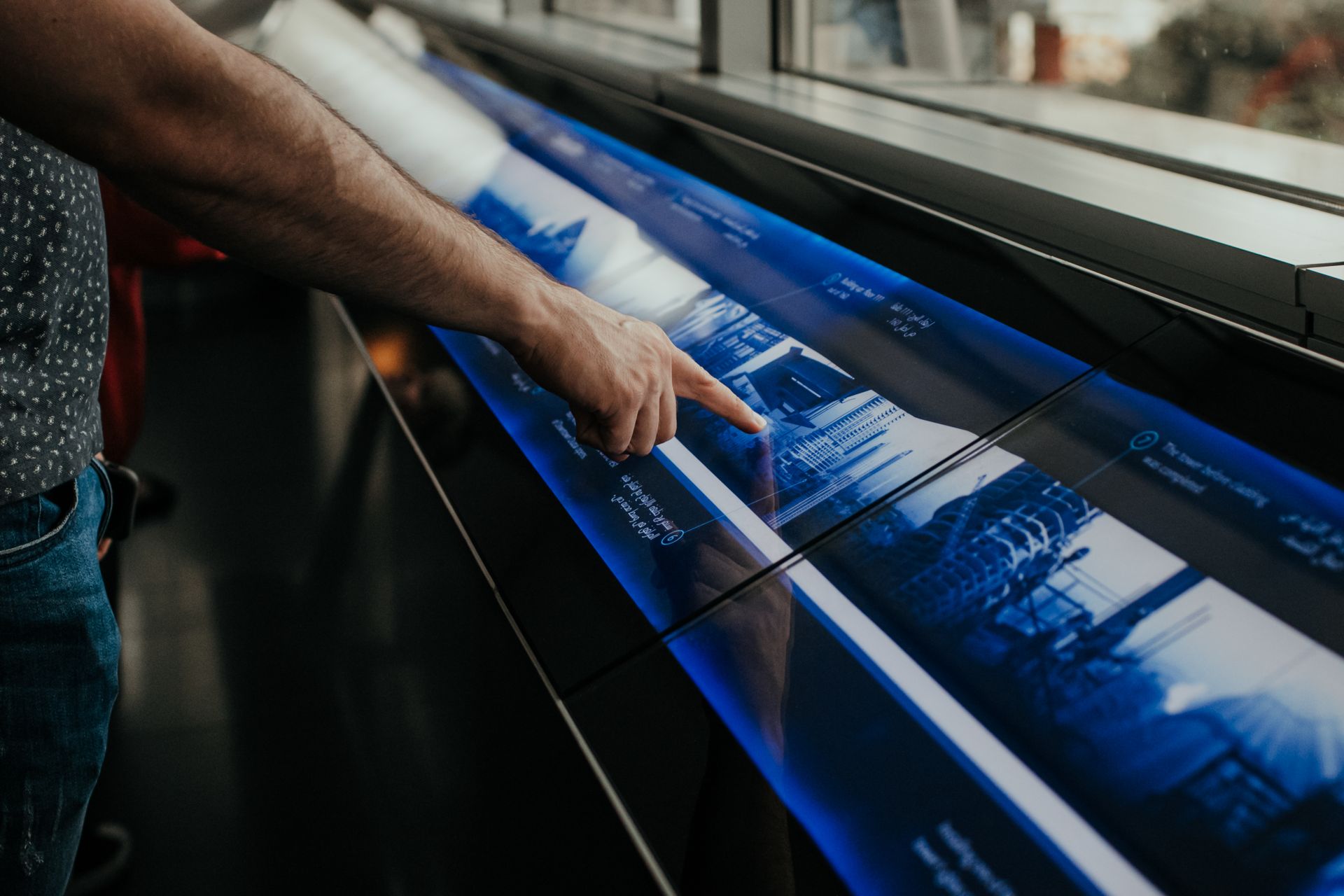 A person touching a large interactive screen displaying photographs of buildings.