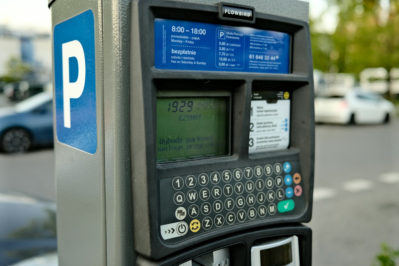 A parking payment machine with a blue P sign, display and letter and number keypad beside parked cars.