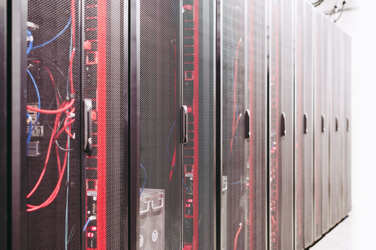 Server racks with mesh cabinet doors and red and blue network cables.