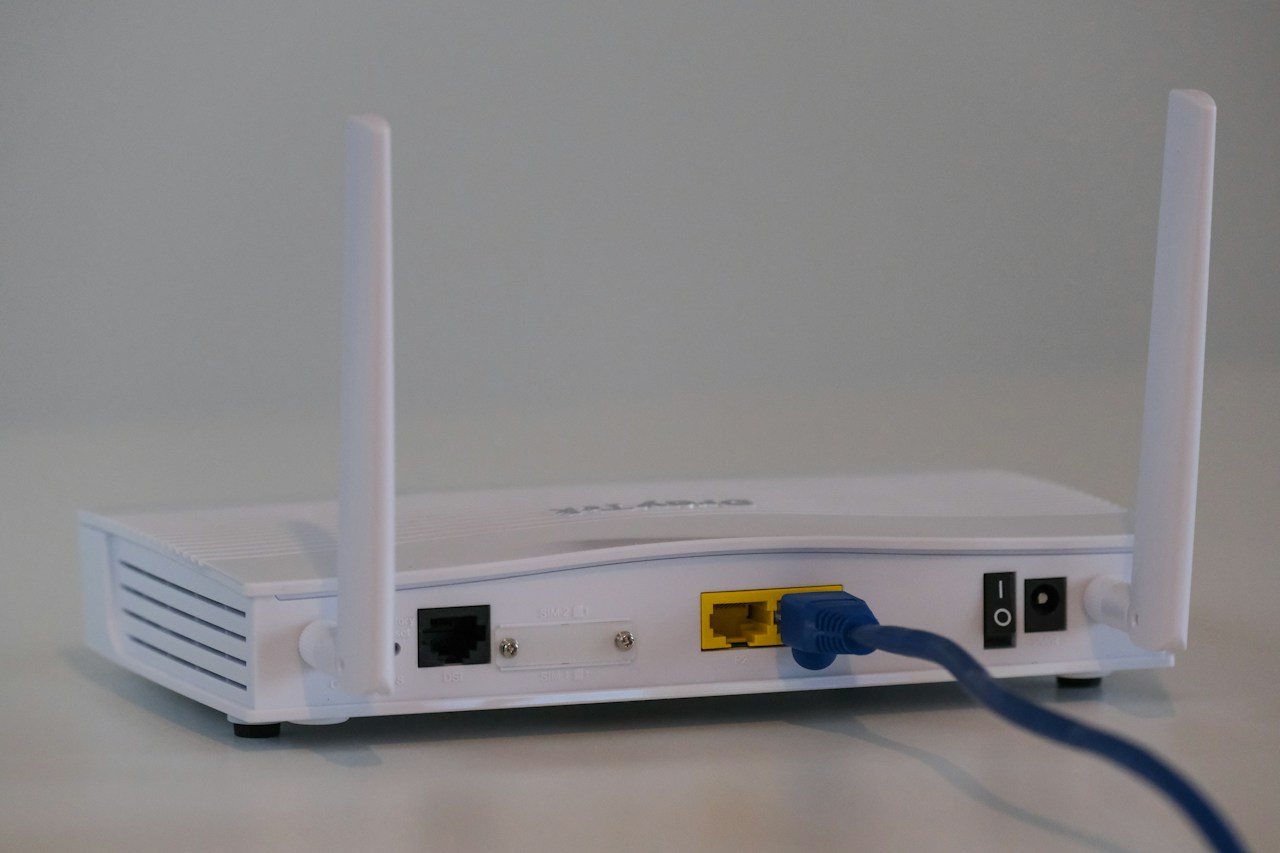 A white router with two upright antennas and a blue Ethernet cable plugged into a yellow port.