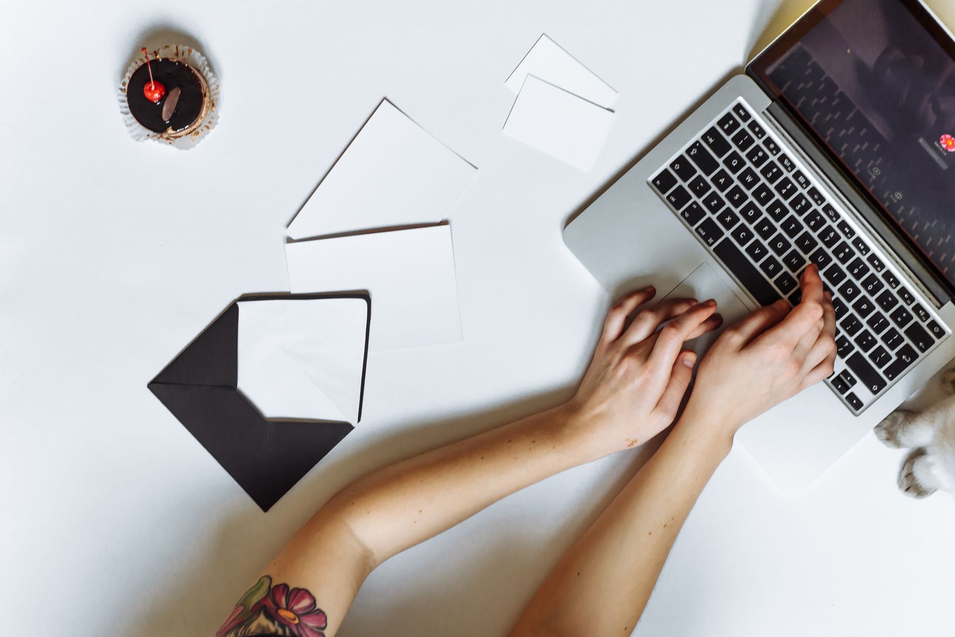 Hands using a laptop beside blank envelopes on a white table.
