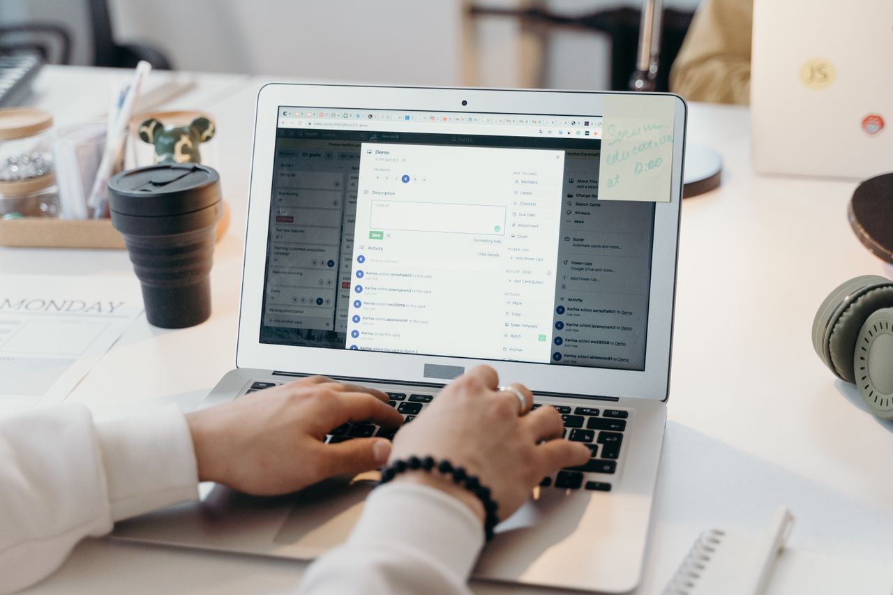 Hands typing on a laptop with a web application open, beside a travel cup and headphones.