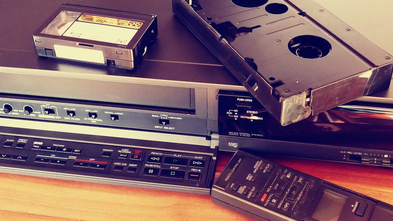 A videocassette recorder with a compact tape, cassette adapter and remote control on a wooden surface.