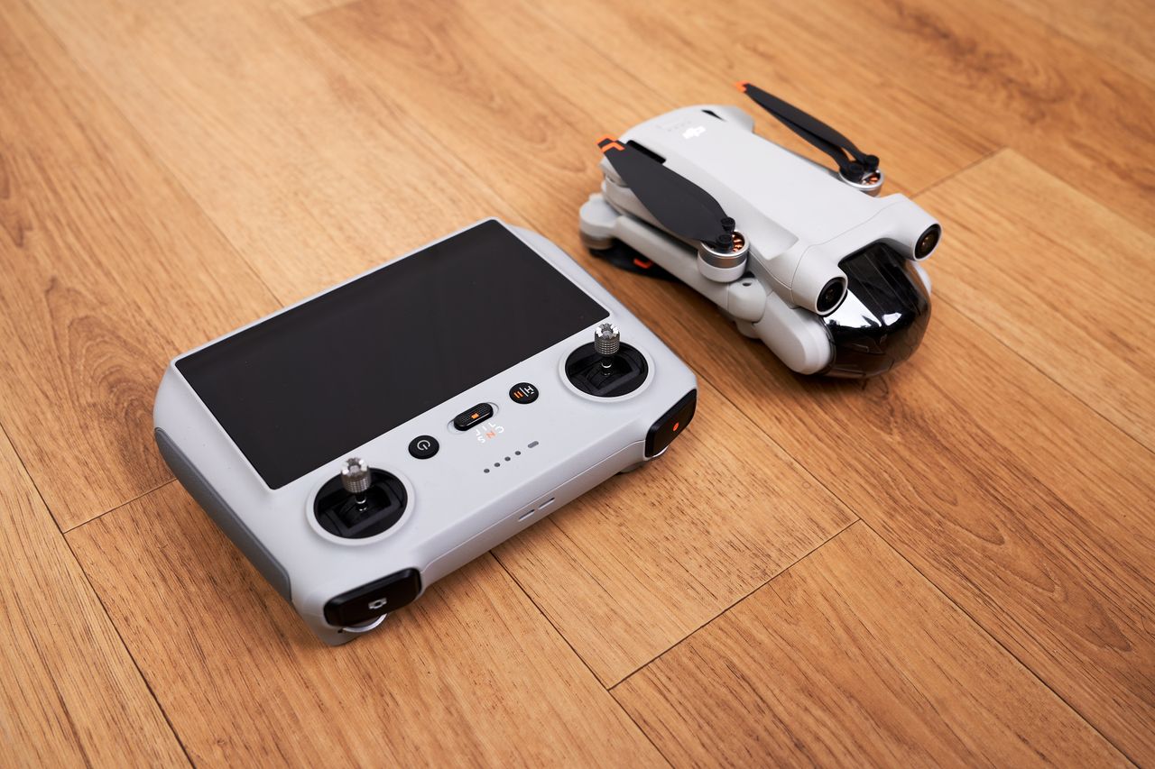 A folded gray camera drone and a controller with a dark screen resting on a wooden surface.