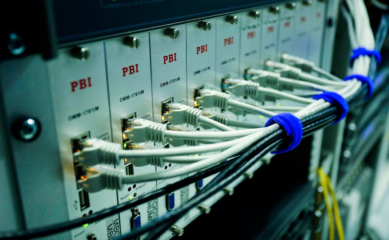 White network cables connect to equipment in a rack, with cable bundles held by blue straps.