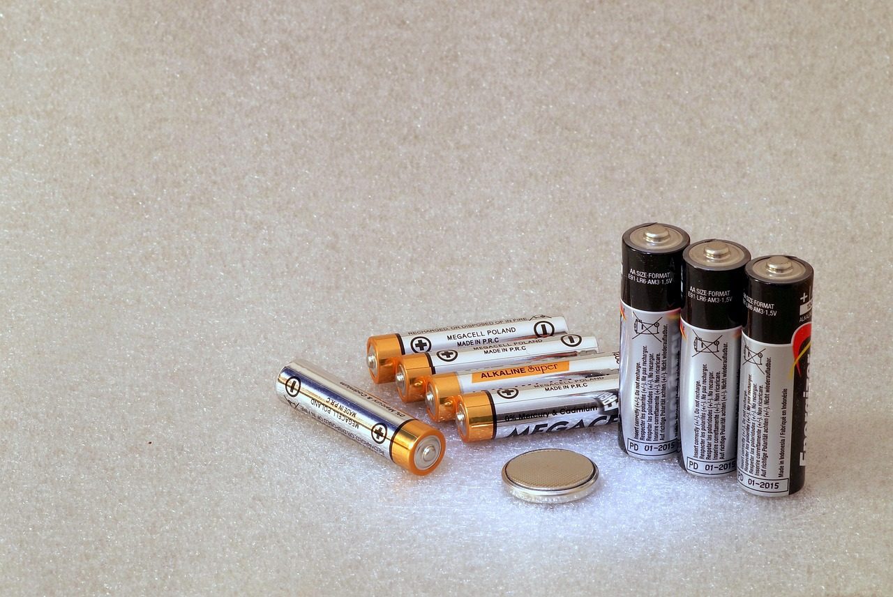 Cylindrical batteries and a flat coin battery rest on a light textured surface.